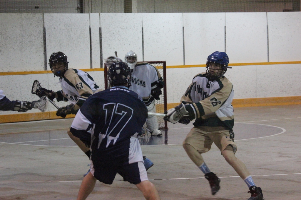 Menschen mit Helmen und Stöcken scheinen in einem Innenraum mit einem Netz im Hintergrund zu kämpfen.
