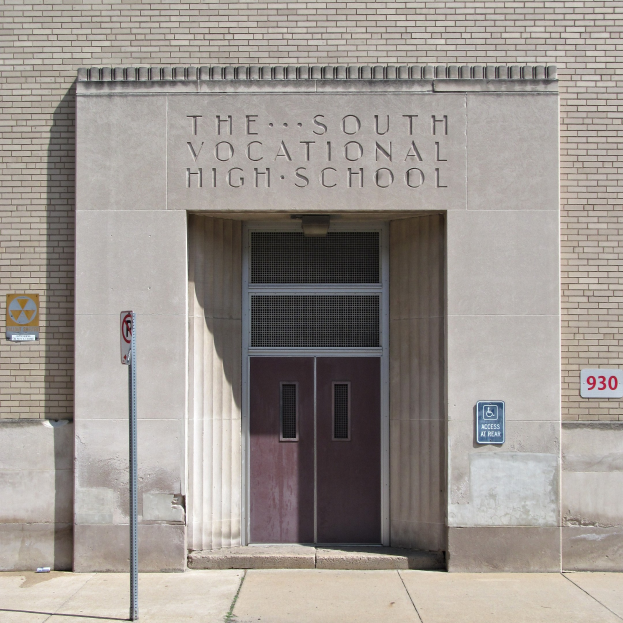 Außensicht der Südberufsschule mit einer Tür, Schildern und einem Weg, der zur Eingangstür führt.