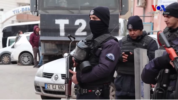 Eine Gruppe von Polizisten in Uniformen mit Waffen steht auf einer Straße in Ankara, Türkei, während einer anti-regierungsamtlichen Demonstration, mit Fahrzeugen, Menschen, Gebäuden und Texttafeln im Hintergrund.
