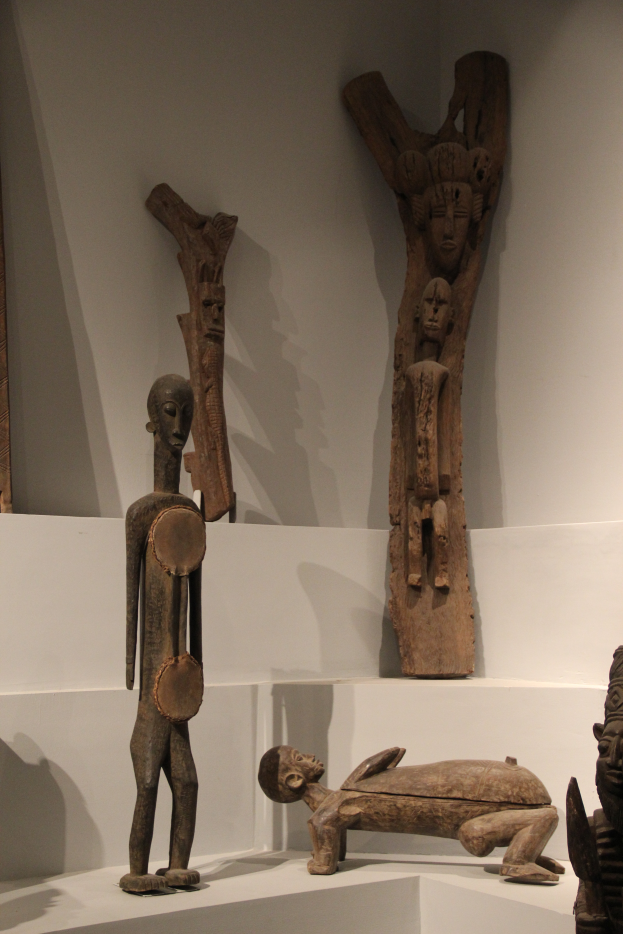 Eine Gruppe von Holzskulpturen, die auf einer weißen Oberfläche in einem Museum ausgestellt sind, mit einer Wand im Hintergrund.