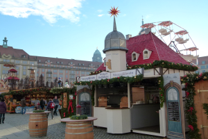 Ein geschäftiger Weihnachtsmarkt in Nürnberg, Deutschland mit Menschen um geschmückte Stände, festliche Lichter, ein Riesenrad, Gebäude und ein Schild im Hintergrund.