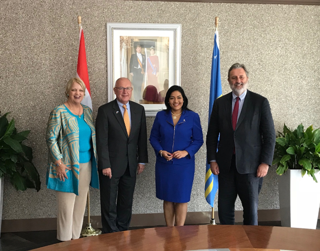 Eine Gruppe strahlender Menschen um einen Tisch mit Papieren herumstehend, umgeben von Fahnen, Topfpflanzen und einem Foto auf der Wand, feiern die Unterzeichnung eines Memorandums zwischen den Vereinigten Staaten und Kanada.