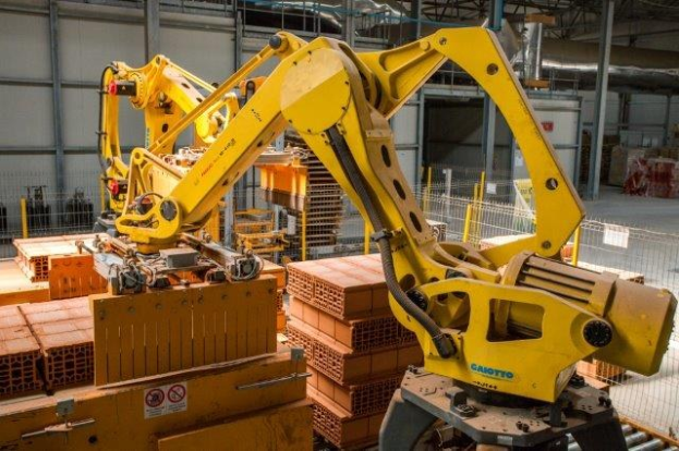 Großes Industrie-Lager mit gestapelten Kisten, Überhead-Kränen, Zaun, Pfählen und einer fernen Wand in einer automatisierten Fertigungsumgebung.