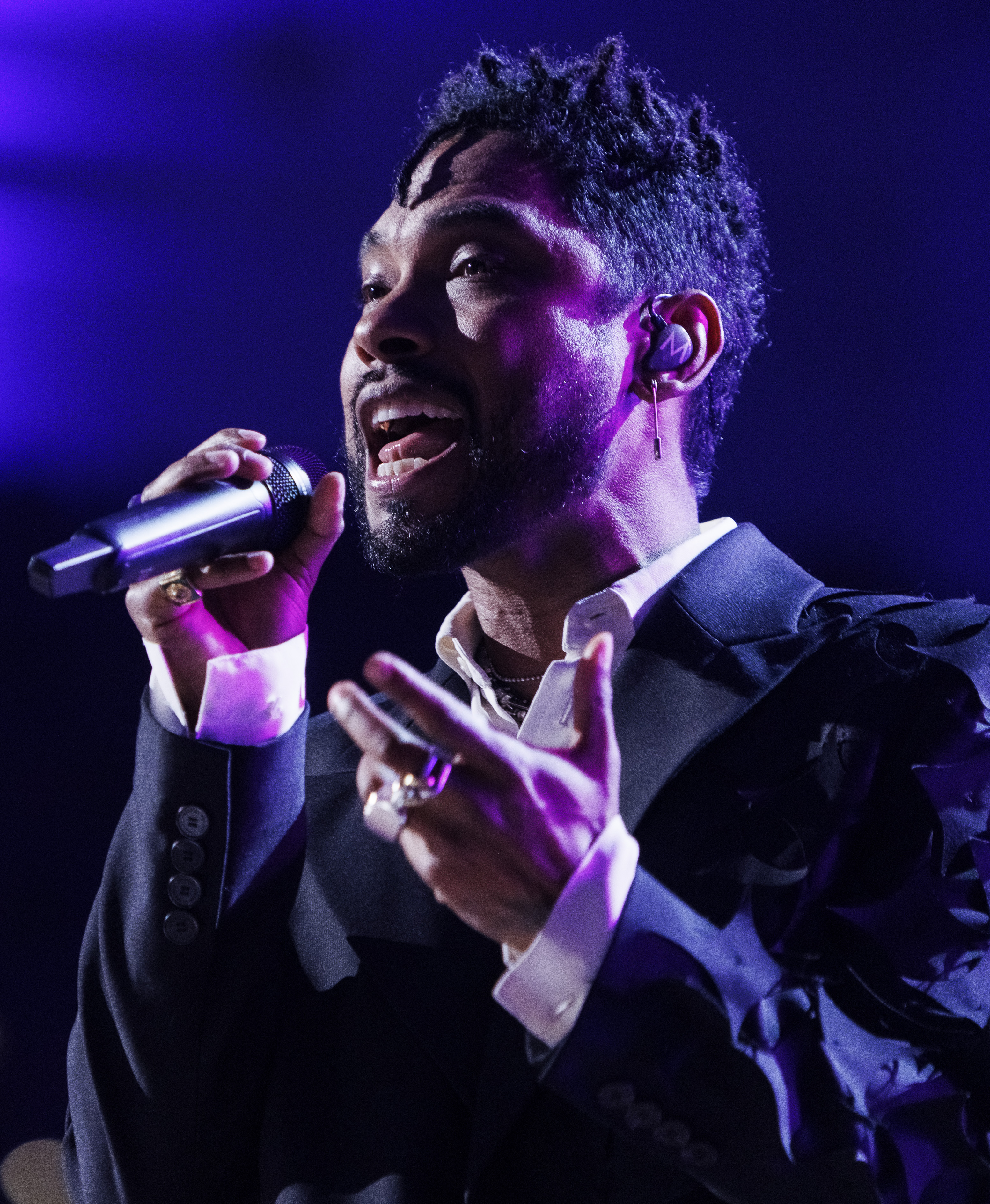 Chadwick Boseman in einem schwarzen Anzug, der in ein Mikrofon singt, mit einem unscharfen Hintergrund.