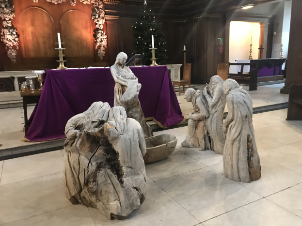Krippe in einer Kirche mit Statuen, einem geschmückten Weihnachtsbaum, Stühlen, einem Tisch mit Kerzen und einem tischgedeckten Tisch.