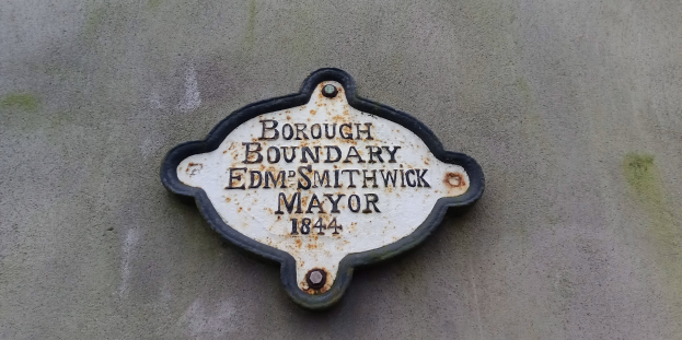 Metallplakette an einer Gebäudeseite mit schwarzem Hintergrund und weißer fettgedruckter Schrift, die "Stadtbezirk Edm Smithwick Bürgermeister" liest.