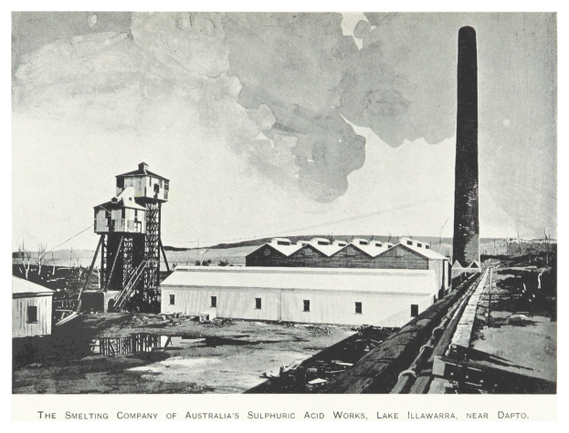 Schwarzes und weißes Foto einer Fabrik mit mehreren Gebäuden, einem hohen Turm und Rauch, der aus einem Schornstein aufsteigt, mit Text unten.