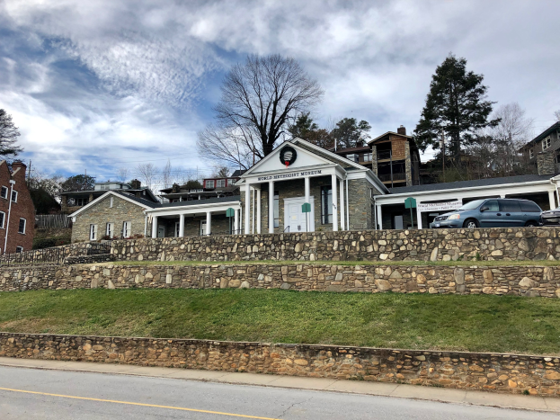 Steinwand mit parkenden Autos, benachbarte Gebäude mit Fenstern und Türen, Bäume und ein bewölkter Himmel, als Weltkulturerbe-Museum bezeichnet.