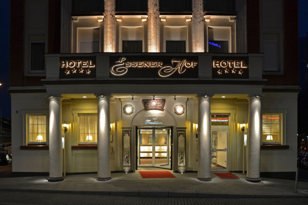 Das Essenerhof Hotel in Berlin, Deutschland, ein mehrstöckiges Gebäude mit Fenstern, Türen, Säulen und einem Namensschild, das sich entlang einer Straße mit Fahrzeugen auf der rechten Seite und einem klaren Himmel im Hintergrund befindet.