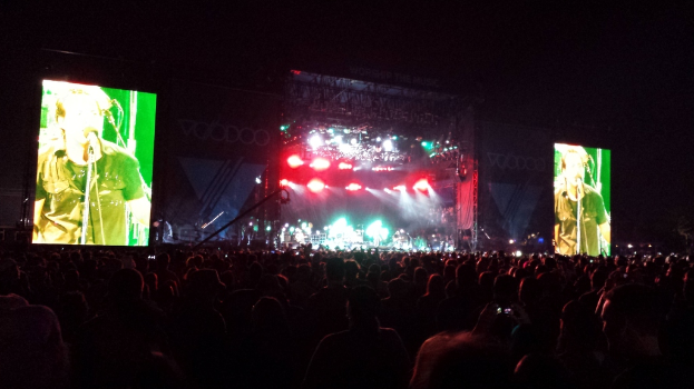 Ein Konzertbild mit einer Menschenmenge unten, einem großen Bildschirm links und einem weiteren Bildschirm rechts.