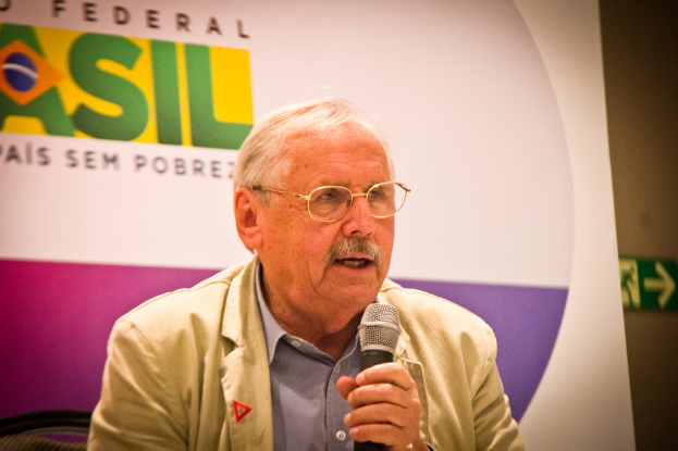 Eine Person, die in ein Mikrofon spricht und hinter sich ein Banner mit dem Wort 'Bundes' trägt.