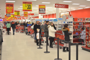 Ein volles Walmart-Geschäft mit Einkaufswagen schiebenden Kunden, umgeben von Warenauslagen, Schildern und Deckenleuchten, wahrscheinlich während eines Black Friday-Verkaufs.