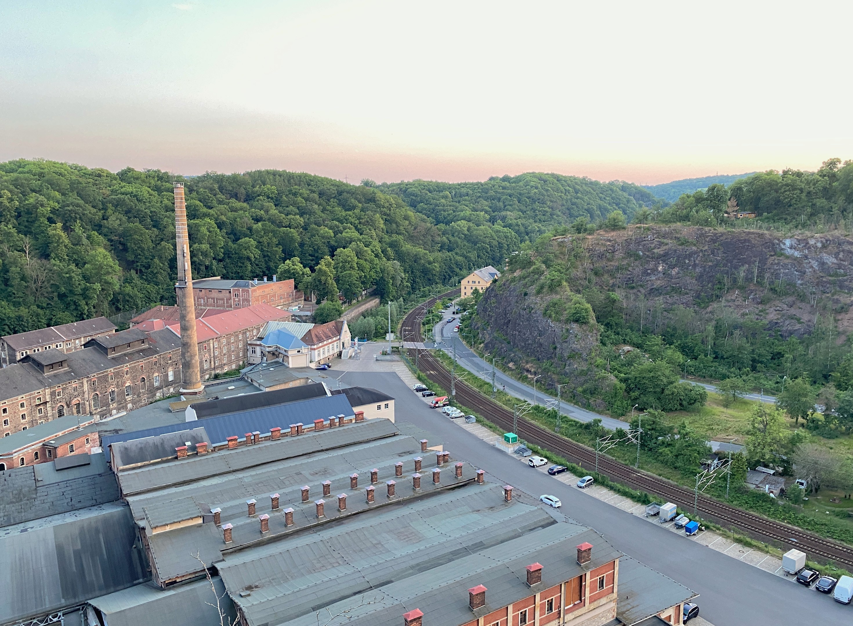 Luftaufnahme einer Stadt mit dichtem Gebäudebestand, Straßen voller Fahrzeuge, Strommasten, Bäumen, umliegenden Hügeln und einem bewölkten Himmel, die an ein Kohlerevier erinnert.