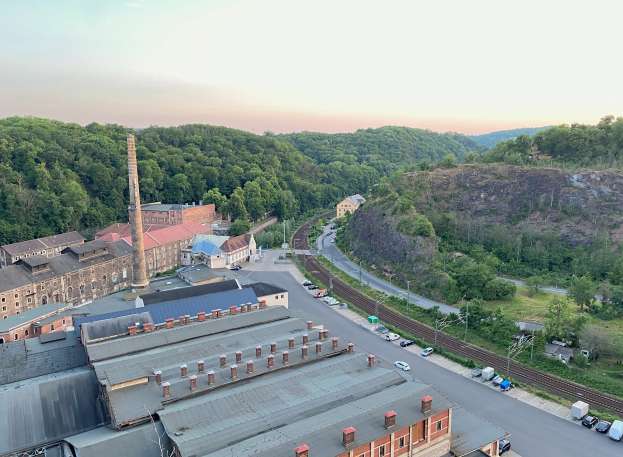 Luftaufnahme einer Stadt mit dichtem Gebäudebestand, Straßen voller Fahrzeuge, Strommasten, Bäumen, umliegenden Hügeln und einem bewölkten Himmel, die an ein Kohlerevier erinnert.