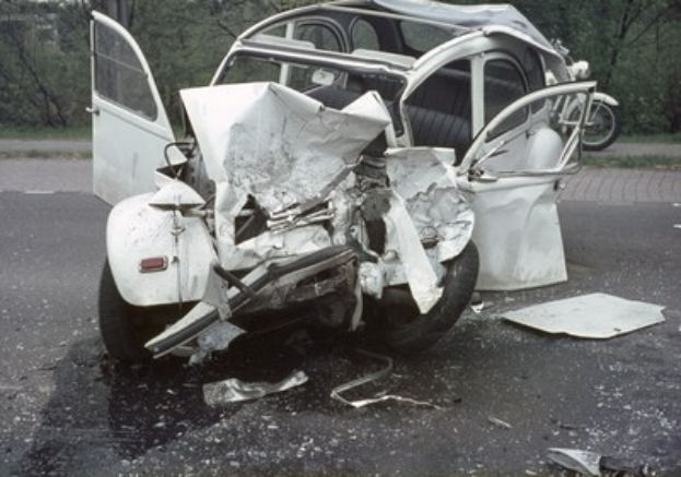 Ein schwer frontbeschädigt aussehender Pkw am Straßenrand mit Bäumen und einem Gebäude im Hintergrund und ein weiteres Fahrzeug in der Ferne.