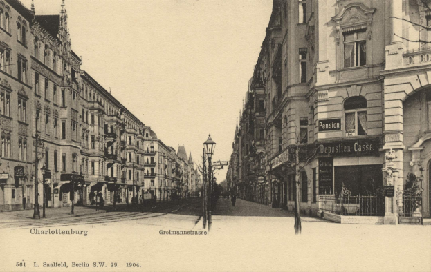 Schwarzes und weißes Foto einer Stadtstraße in Charlottenburg, Deutschland, mit Gebäuden, Straßenlaternen, Lampen, Namensschildern, Kraftfahrzeugen, Fußgängern, Gittern und einem klaren Himmel.