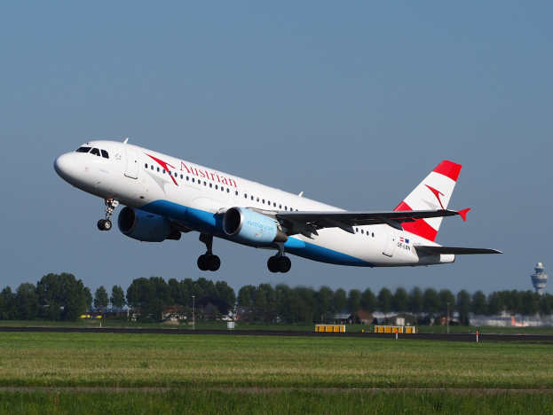 Airbus A320-200 der Austrian Airlines startet von Frankfurt Airport mit grünem Gras darunter, Bäumen und Gebäuden im Hintergrund und einem Turm auf der rechten Seite.