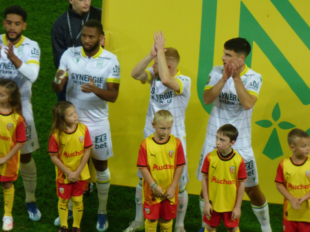Eine Gruppe von Fußballspielern in Uniformen klatscht feierlich auf einem Ligue 1-Feld, mit einem "Ligue 1" Schild im Hintergrund.