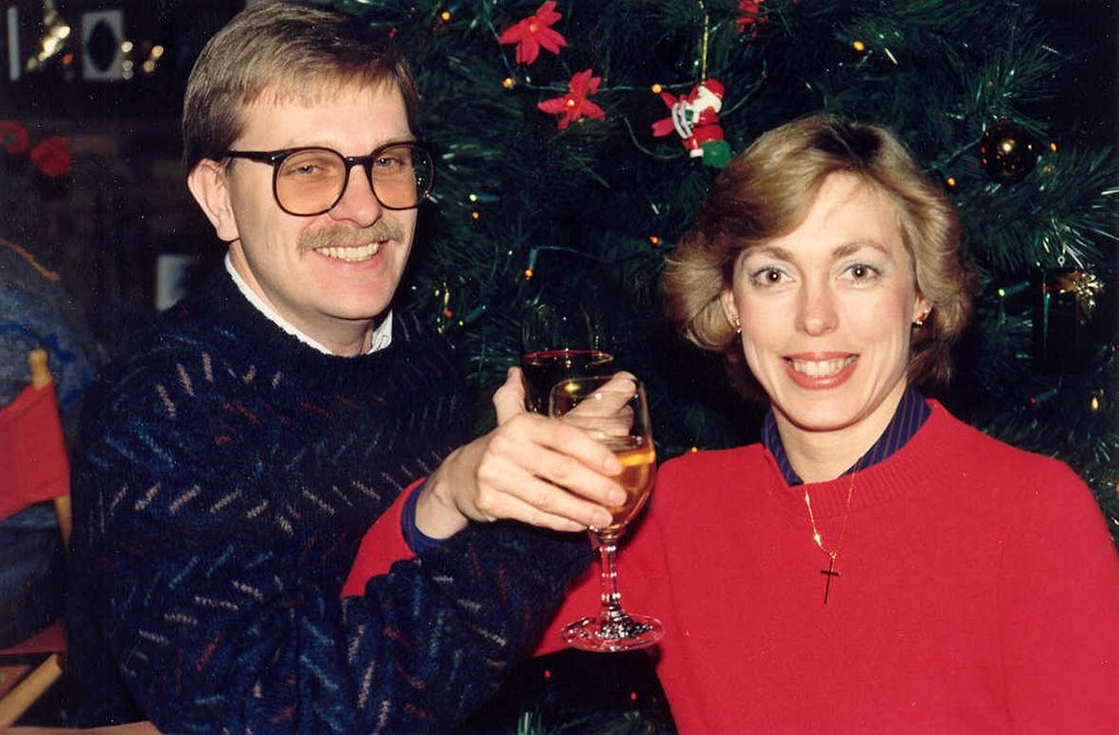 Ein Paar lächelt, während es Gläser mit Wein hält, mit einem Weihnachtsbaum im Hintergrund.