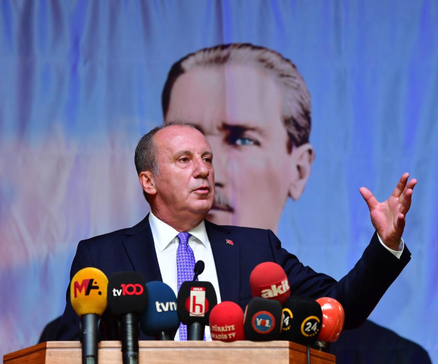 Ein Mann im Anzug steht an einem Podium mit Mikrofonen und spricht hinter einem Bildschirm, wahrscheinlich zu den Nachrichten über den Rücktritt des türkischen Präsidenten Recep Tayyip Erdogan.