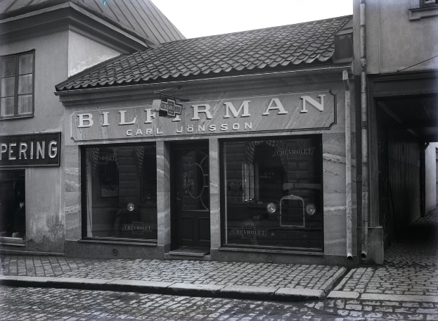 Ein Schwarz-Weiß-Foto eines Gebäudes mit einer "Bilferman"-Aufschrift, Fenstern, einer Tür und Schildern mit Text, sowie einer Straße unten.