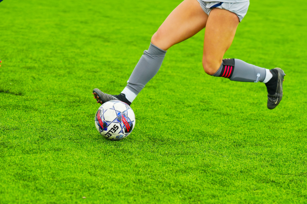 Eine Frau in Sportbekleidung und -schuhen tritt einen Fußball auf einem saftigen grünen Feld.