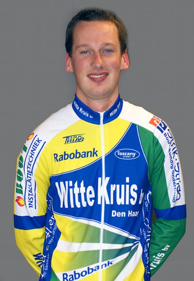 Ein männlicher Athlet posiert für ein Foto, trägt ein Shirt mit mehreren Sponsoren-Logos.