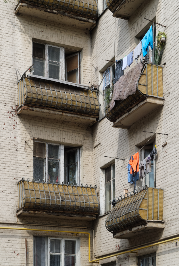 Ein Wohnhaus mit Fenstern, Balkonen, Wäsche zum Trocknen und an der Seite verlaufenden Rohren.