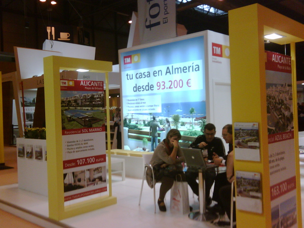 Ein Raum mit Menschen, die an einem Tisch arbeiten, umgeben von Flyern mit verschiedenen Werbeaussagen.