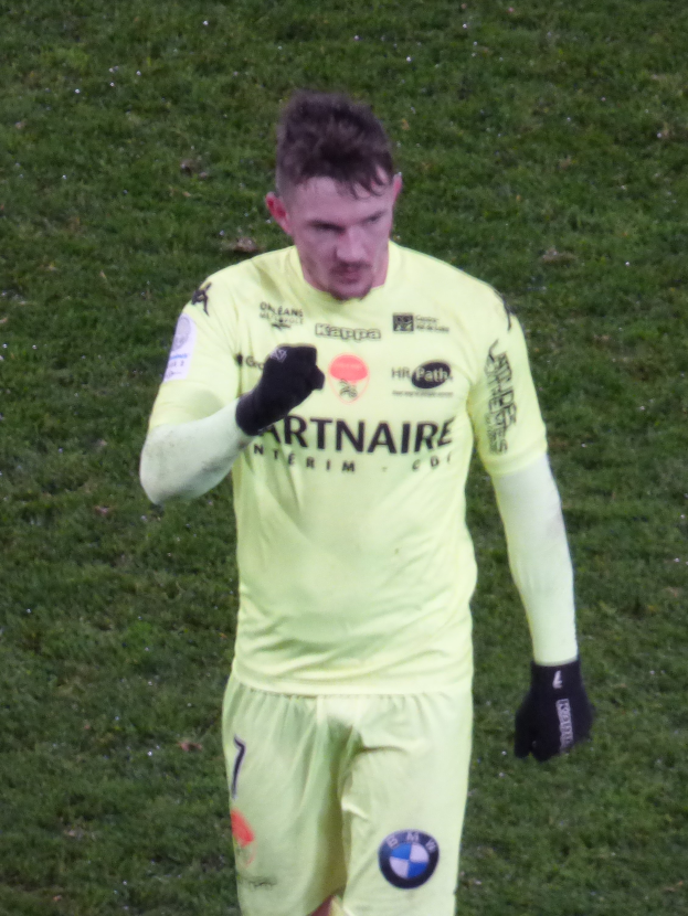 Ein Mann in einem gelben Torwarttrikot, einschließlich T-Shirt, Shorts und schwarzen Handschuhen, steht auf einem Fußballfeld.