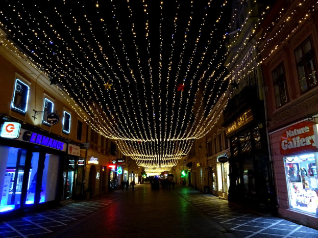 Eine nächtliche Stadtstraße mit Weihnachtsbeleuchtung, mit Gebäuden auf beiden Seiten und ein paar Menschen, die den Weg entlanggehen.