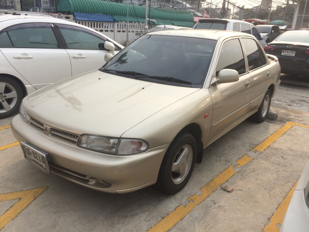Goldfarbenes Auto auf einem Parkplatz neben anderen Autos geparkt, umgeben von Gebäuden, Polen, Drähten, Bäumen und einem klaren blauen Himmel.