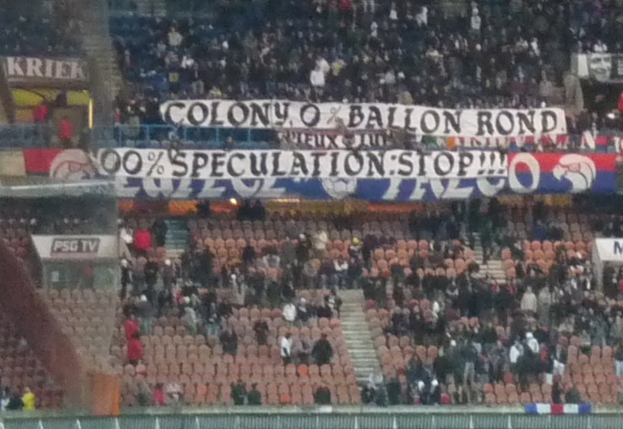 Ein Stadion voller Menschenmassen, Banner und Stühle, mit einem Zaun unten und einer Treppe links.