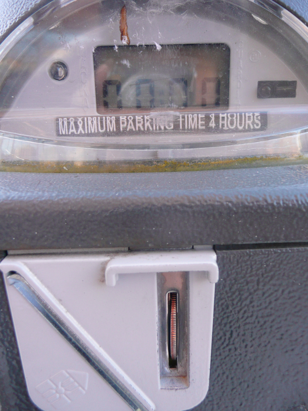 Ein Parkscheinautomat mit der Aufschrift "Maximale Parkdauer 4 Stunden" und einem Münzschlitz mit einer Münze.