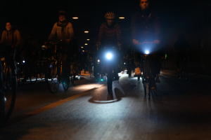 Eine Gruppe von Menschen, die nachts mit Fahrrädern eine Stadtstraße hinunterfahren und Helme tragen.