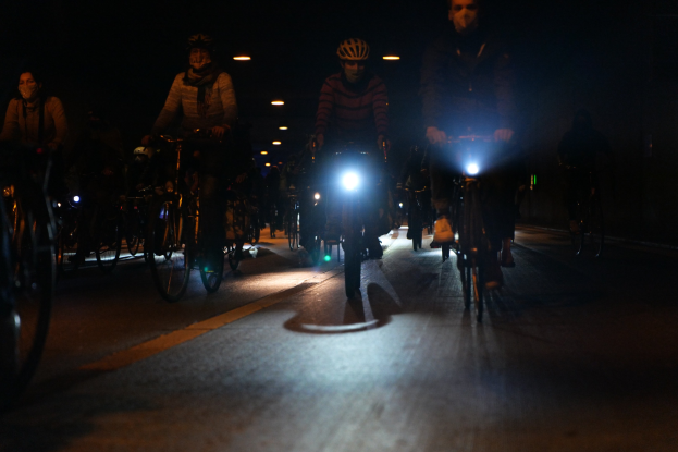 Eine Gruppe von Menschen, die nachts mit Fahrrädern eine Stadtstraße hinunterfahren und Helme tragen.