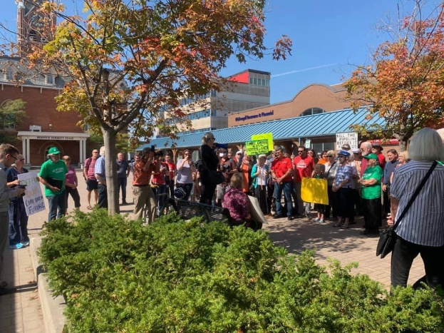 Eine Gruppe von Studenten protestiert vor einem Gebäude auf dem Campus der University of Michigan, hält Schilder und trägt einige Kameras und Taschen.
