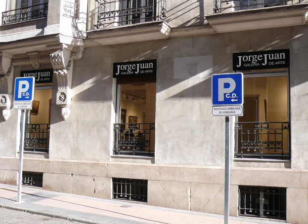 Ein mehrstöckiges Gebäude mit Fenstern, Geländern, Türen und Säulen, das Schilder an Pfosten entlang des Gehwegs und sichtbare Innenobjekte zeigt, die auf eine belebte städtische Umgebung hinweisen.