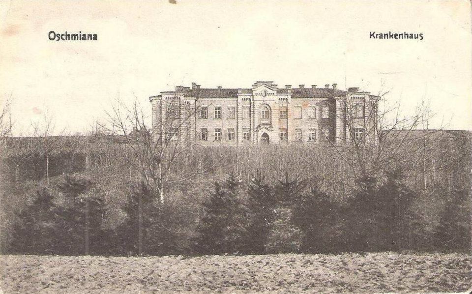 Ein altes Schwarz-Weiß-Foto eines großen Gebäudes, Schloss Oschmiana, in einem von Bäumen umgebenen Feld, mit der Aufschrift "Oschmiana Castle in Krankenhaus" oben und unten.
