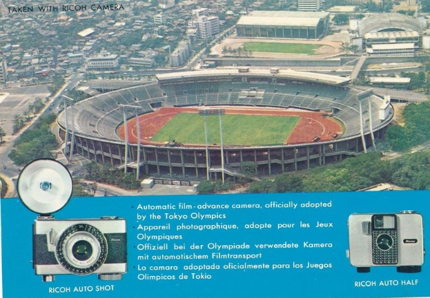 Luftaufnahme eines Stadions mit einer Kamera im Vordergrund, umgeben von Gebäuden, Bäumen und Fahrzeugen, mit einem Plakat der Kamera unten.