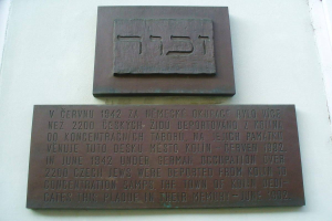 Metal plaque with Hebrew text mounted on the side of a building, likely a memorial for the Jewish community.