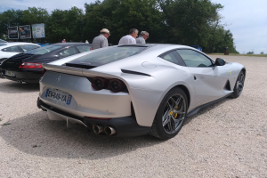 Roter Ferrari 812 Superfast auf dem Goodwood Festival of Speed, umgeben von Menschen mit Käpfen, Bäumen, Texttafeln und einem bewölkten Himmel im Hintergrund.