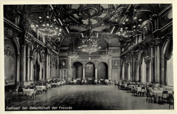 Schwarzes und weißes Foto eines großen Raums mit Tischen, Stühlen, Säulen, Bögen und Kronleuchtern an der Decke, beschriftet mit "Fest der Gesellschaft der Freunde, Berlin" unten.