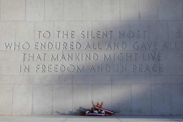 Eine Gedenkwand mit der Inschrift "Dem stillen Heer, das alles ertrug und alles gab, damit die Menschheit in Freiheit und Frieden leben möge", geschmückt mit einem Blumenstrauß.