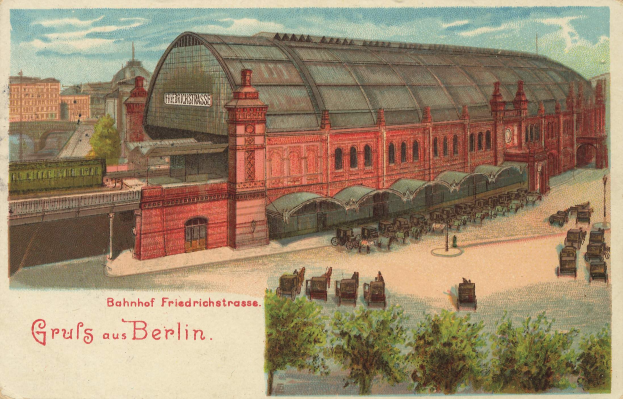Schwarz-weiß-Postkarte eines alten Berliner Bahnhofs mit einem Gebäude, Bäumen, Karren, Menschen, einer Brücke und einem bewölkten Himmel, mit Text unten.