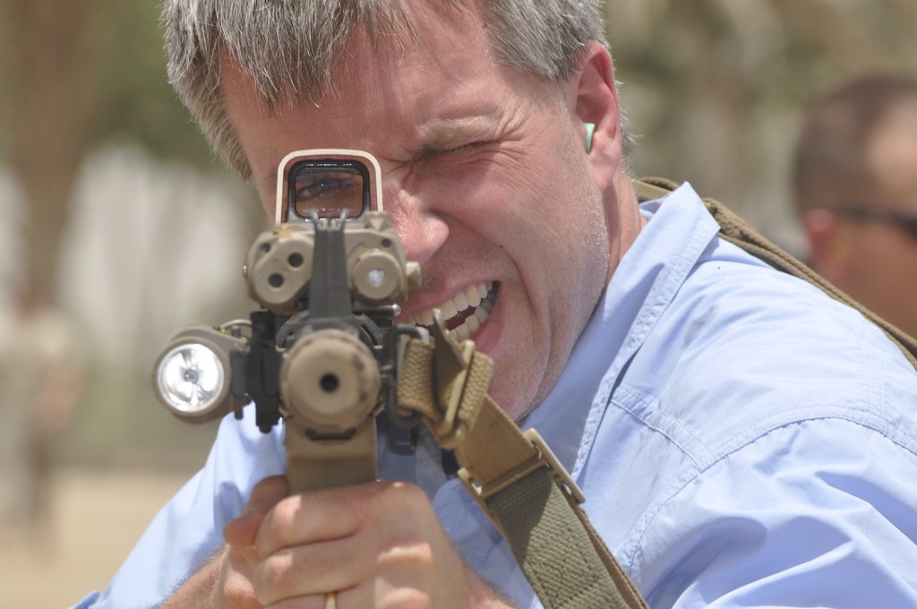 Ein Mann in einem himmelblauen Hemd, der eine Waffe hält, mit einem unscharfen Hintergrund.