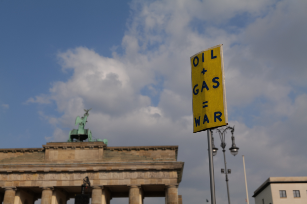 Das Brandenburger Tor in Berlin, Deutschland, mit einem gelben Schild, auf dem "Öl und Gas Krieg" steht, Gebäuden, Polen, Lampen, einer Statue und einem bewölkten Himmel im Hintergrund.