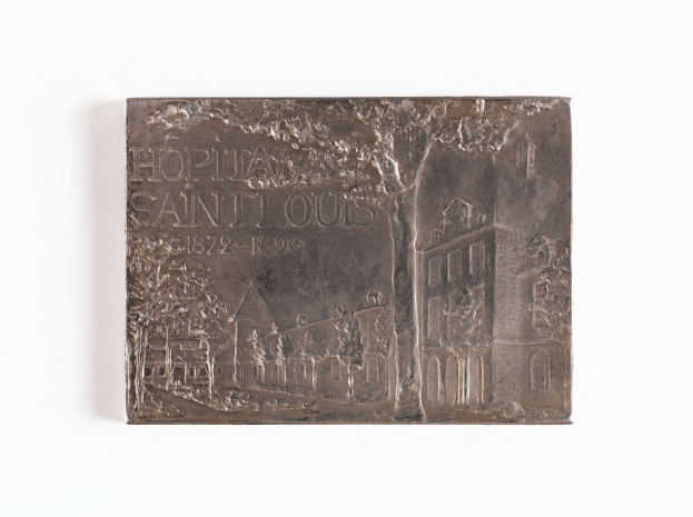 Eine silberne Plakette mit einem Bild eines Gebäudes und dem Text "Krankenhaus Saint Louis" auf einem weißen Hintergrund.