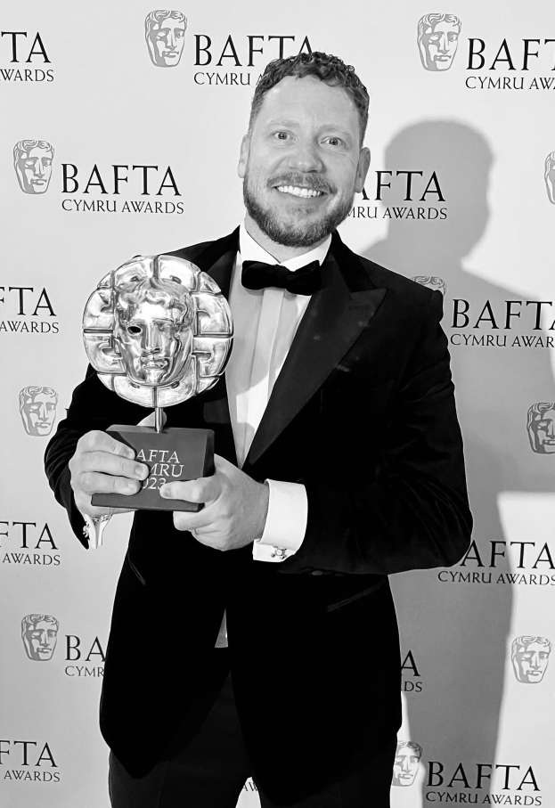 Ein Mann im Smoking steht lachend und hält einen BAFTA-Award in der Hand, vor einem Hintergrund mit der Aufschrift "BAFTA Awards 2018."